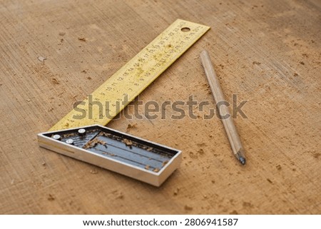 Yellow try square ruler and carpenter pencil on wooden board with sawdust. Woodworking measurement tools, carpentry workshop background, DIY home renovation or construction concept