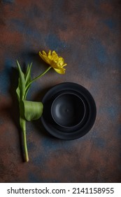 Yellow tulip, black ceramic plate on rust old heavily worn black navy blue concrete texture or background. With place for text and image