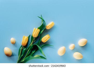 Yellow tulips and Easter eggs on blue background. Top view, flat lay, copy space.