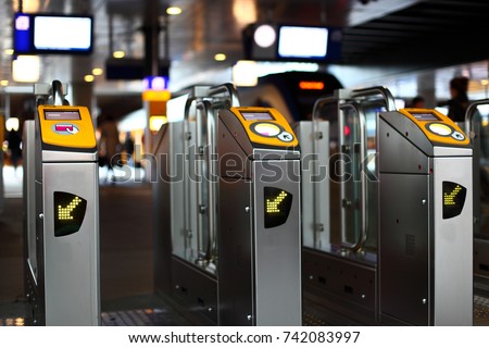 Yellow turnstile or tourniquet on the railway station or underground in city center. Blurred trains and timetable screens on the background