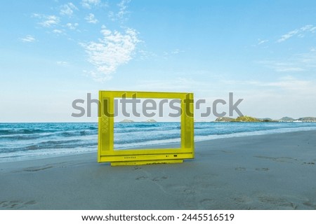 Yellow TV frame on the beach. The blue sky is bright and calm.