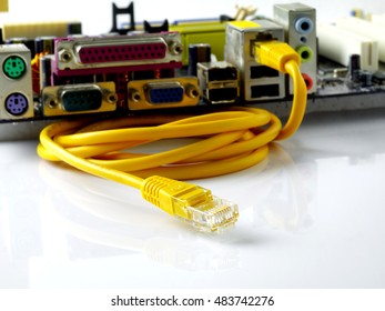 yellow twisted pair ethernet network cable connected to dismounted motherboard, closeup, white background, focus on unplugged network connector