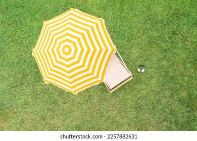 Yellow umbrella with deck chair on the green grass sunbathes at summer day. Top view, drone, aerial view.