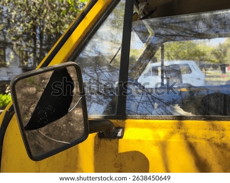 A yellow van with a broken mirror. The reflection of a white car