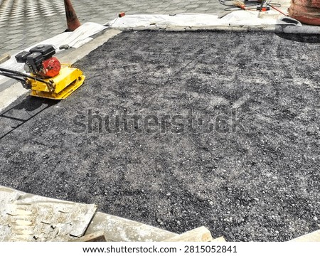 Yellow vibratory plate compactor machine compacting freshly laid asphalt on road repair site outdoors