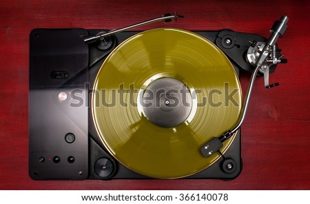 Yellow vinyl record played on a hi-end turntable record player top view standing on red wood stand