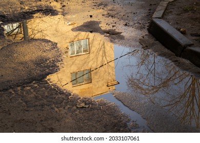 Yellow wall house reflection into water of puddle on damaged asphalt street road after spring melting snow - Powered by Shutterstock