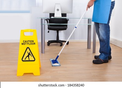 Yellow Warning Notice To Caution People To A Slippery Wet Surface As A Janitor Mops The Floor In An Office Building