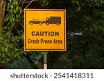 Yellow warning sign board on a roadside pole indicating a crash-prone zone, aimed at alerting drivers of potential danger and promoting road safety.