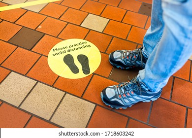 Yellow Warning Sign To Maintain Social Distance Distancing During Covid-19 Coronavirus Outbreak With Footsteps In Store And Legs Of Person In USA