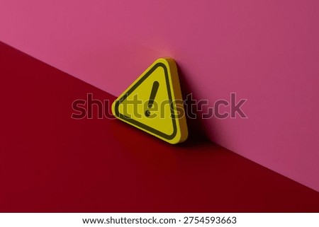 A yellow warning triangle with a black exclamation mark leaning against a pink wall. Caution, error, alerts, hazards, and attention concept. Copy space for text.