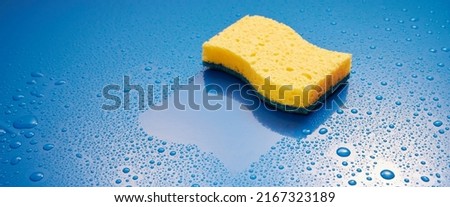 Yellow wash scrub sponge placed on wet blue background covered with drops of water in light room during household chores