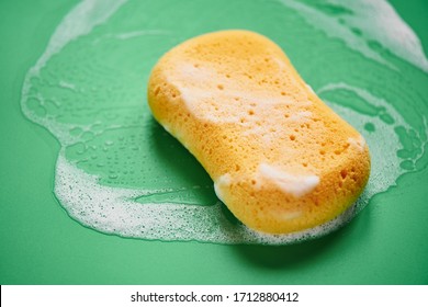 Yellow Washing Sponge In Soap Foam On A Green Background Close Up Isolated