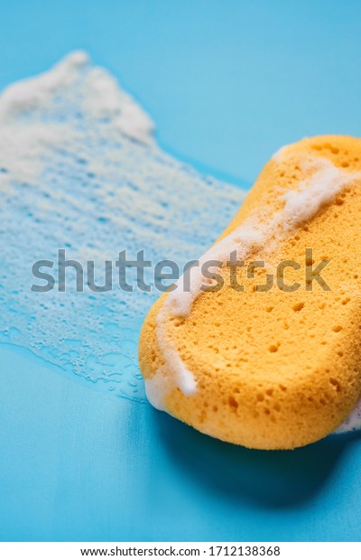 Yellow washing sponge in soap foam on a blue\
background isolated