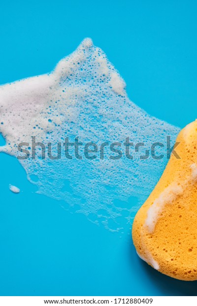 Yellow washing sponge in soap foam on a blue\
background isolated