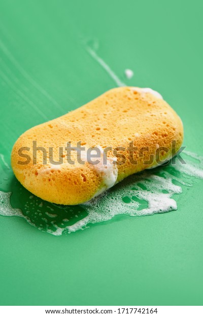 Yellow washing sponge in soap foam on a green\
background close up\
isolated