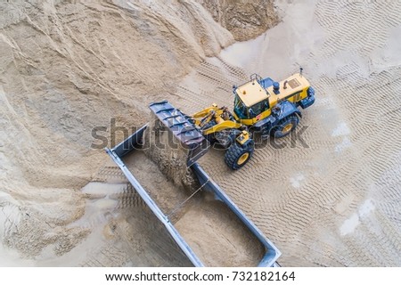 Yellow wheel loader loading sand on dumper truck. Sand quarry