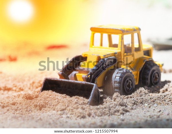 A yellow\
wheel loader toy dinging in the\
sand