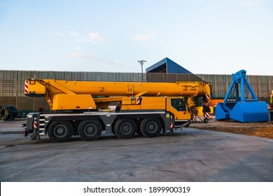 A yellow wheeled truck crane stands in the port of Cartagena, Colombia. Heavy wheeled loading equipment. Next to the truck crane there is a large two-blade bucket for unloading ships.