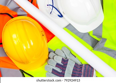 Yellow And White Hard Safety Hats With Protective Gloves And Glasses Laying On A Pile Of Hi Vis Vests