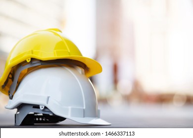 Yellow And White Hard Safety Wear Helmet Hat In The Project At Construction Site Building On Concrete Floor On City With Sunlight. Helmet For Workman As Engineer Or Worker. Concept Safety First. 