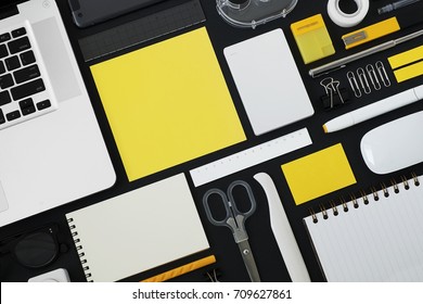 Yellow and white office supplies on black desk table. Top view.