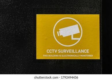 Yellow and white rectangular generic CCTV warning notice sticker on a black wall.