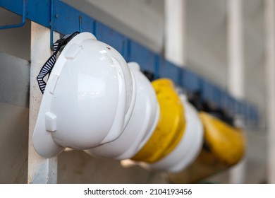 Yellow And White Safety Helmet Which Is Keep At Metal Rail Rack At The Factory Wall, Industrial PPE Object Photo. 