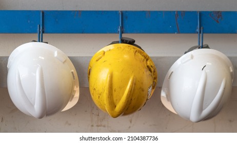 Yellow And White Safety Helmet Which Is Keep At Metal Rail Rack At The Factory Wall, Industrial PPE Object Photo. 