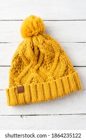 Yellow Winter Hat With Pompon On White Wooden Background. Top View