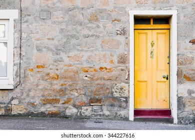 A yellow wooden front door in a stone cottage in Scotland
