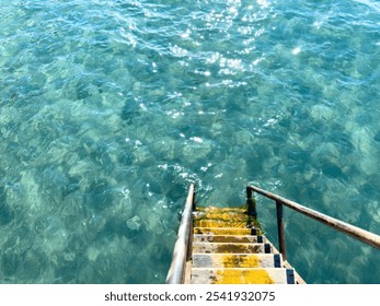 Yellow wooden steps with metal handrails descend into clear turquoise water. Top view creating an atmosphere of calm and relaxation - Powered by Shutterstock