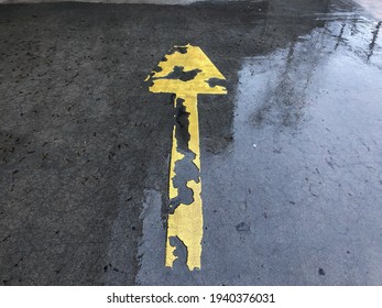 
Yellow Worn Out Sign Arrow On A Wet Parking Lot. Sign. 