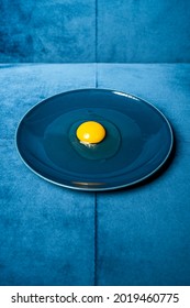 Yellow Yolk And Transparent White Chicken Egg On A Round Blue Plate And Blue Velvet