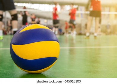 Yellow-blue volleyball on the floor in the gym, team of athletes playing volleyball