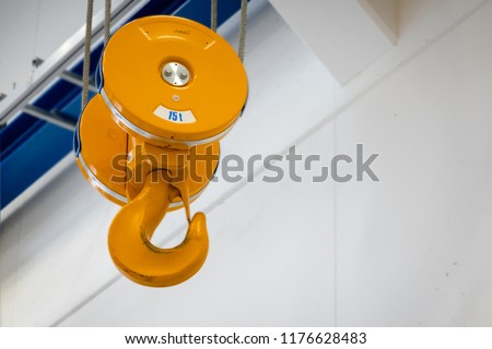 Yellow-painted lifting device consisting of a stable hook and a steel wire rope hoist with a lifting capacity of 15 tons.