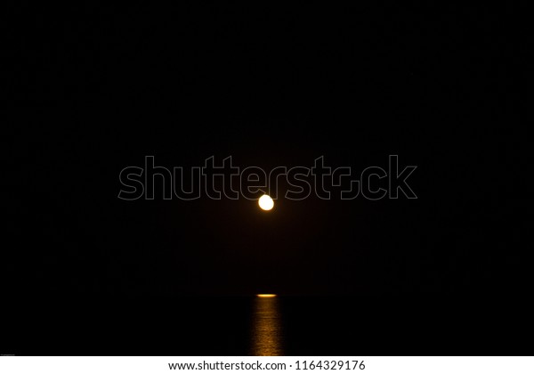 Yellow-red moon rising from the sea  waters  at\
dark hot summer\
night