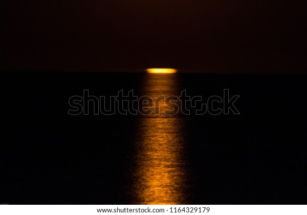 Yellow-red moon rising from the sea  waters  at\
dark hot summer\
night
