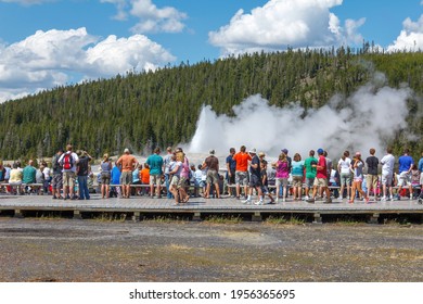 Yellowstone National Park, Montana, USA - July 15 2018: Tourist visitors watching the eruption of the Old Faithful Geyser  with its boiling water and hot steam from underground lava flows by volcano.