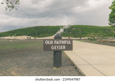 Yellowstone Old Faithful Geyser Sign With Geyser Steaming In The Background Wide Shot Moody Sky