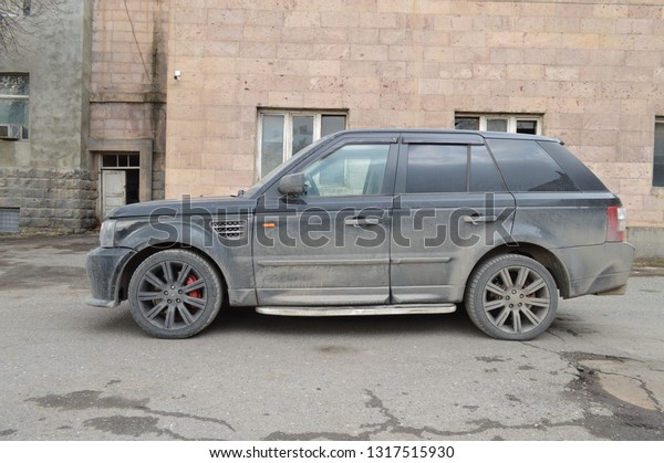 Yerevan, Armenia - 18 February 2019.\
Black and\
dirty Range Rover Sport near the abandoned soviet factory. Dirty\
car, grey walls and nothing else.\
