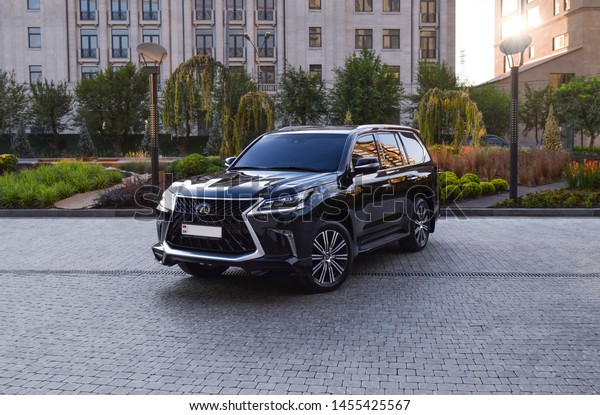 Yerevan, Armenia - 18 July\
2019.\
Dark brand new black luxury Lexus LX570 standing at hotel\
parking near green trees and bushes with modern building on\
background. 