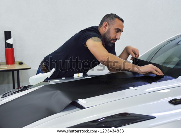 Yerevan, Armenia - 22 January 2019.\
Man\
with beard wrapping vinyls on american car Ford Mustang. Silver\
sport car gonna be with black and red stripes.\
