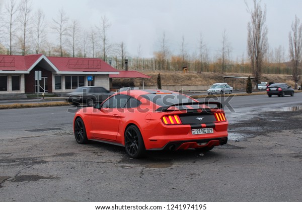 Yerevan, Armenia -\
28 March 2018.\
Orange Ford Mustang with black stripes at highway\
surrounded with rainy\
weather