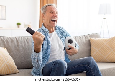 Yes. Excited Mature Man Watching Football Match, Shaking Clenched Fist. Emotional Guy Sitting On Couch Cheering Favorite Team Enjoying Game Goal On TV Holding Remote Controller And Soccer Ball