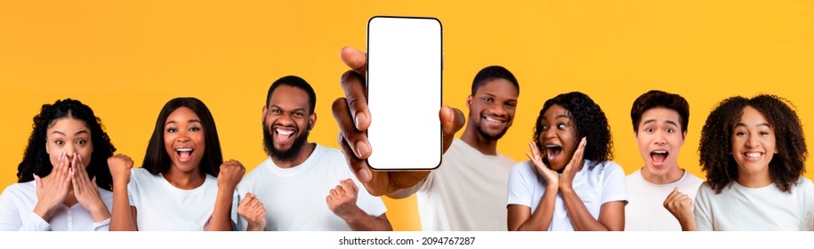 Yes, Great Offer. Excited Multiracial Peope Holding Big Smartphone With Empty White Cell Screen In Hand, Shaking Clenched Fists, Cheerful Diverse Friends Celebrate Win, Yellow Orange Studio Background