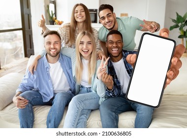 Yes, Great Offer. Excited Multiracial Peope Holding Big Smartphone With Empty White Cell Screen In Hand, Showing V Victory Peace Sign Gesture, Cheerful Friends Celebrate Win Sitting On Couch At Home