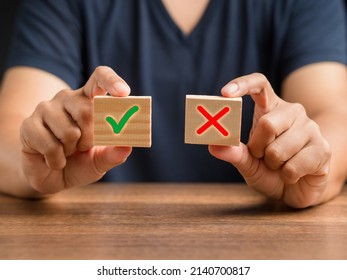 Yes or No. Hand holding two wooden cubes with a green checkmark and red cross. True and false symbols accept rejected for evaluation. Close-up photo - Shutterstock ID 2140700817