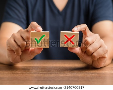 Yes or No. Hand holding two wooden cubes with a green checkmark and red cross. True and false symbols accept rejected for evaluation. Close-up photo