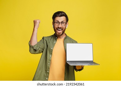 Yes. Overjoyed Middle Aged Man Holding Pc Laptop With Blank Screen And Shaking Clenched Fists, Making Winner Gesture, Showing Device With Empty Space For Mockup, Yellow Background